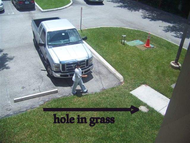Hole in grass covered with sand next to sidewalk.