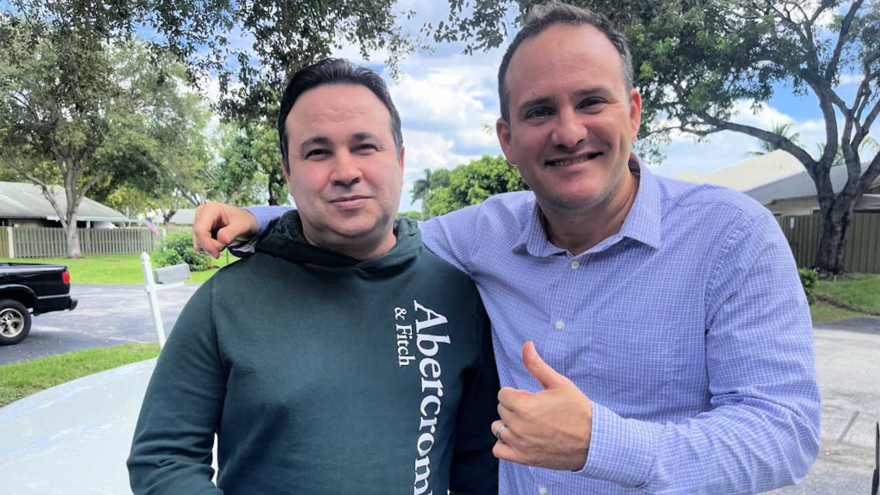 Injury lawyer Justin Ziegler smiling with his client outside after successfully settling his personal injury case. The client stands next to him, looking content. Trees and a residential neighborhood are visible in the background.