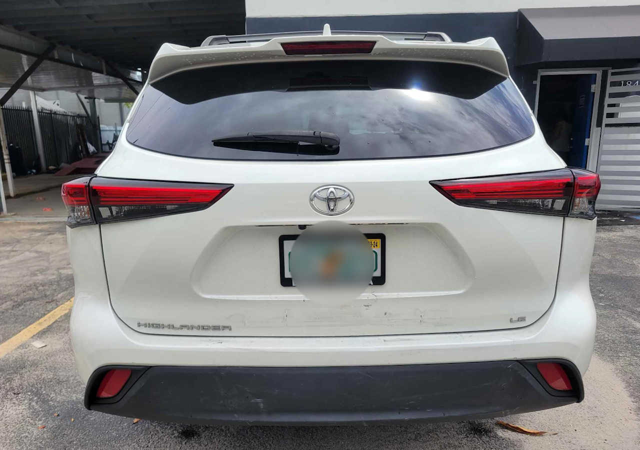 rear view of a white Toyota Highlander LE SUV parked outside a building, showing a clean bumper with minor scuff marks and a blurred license plate.